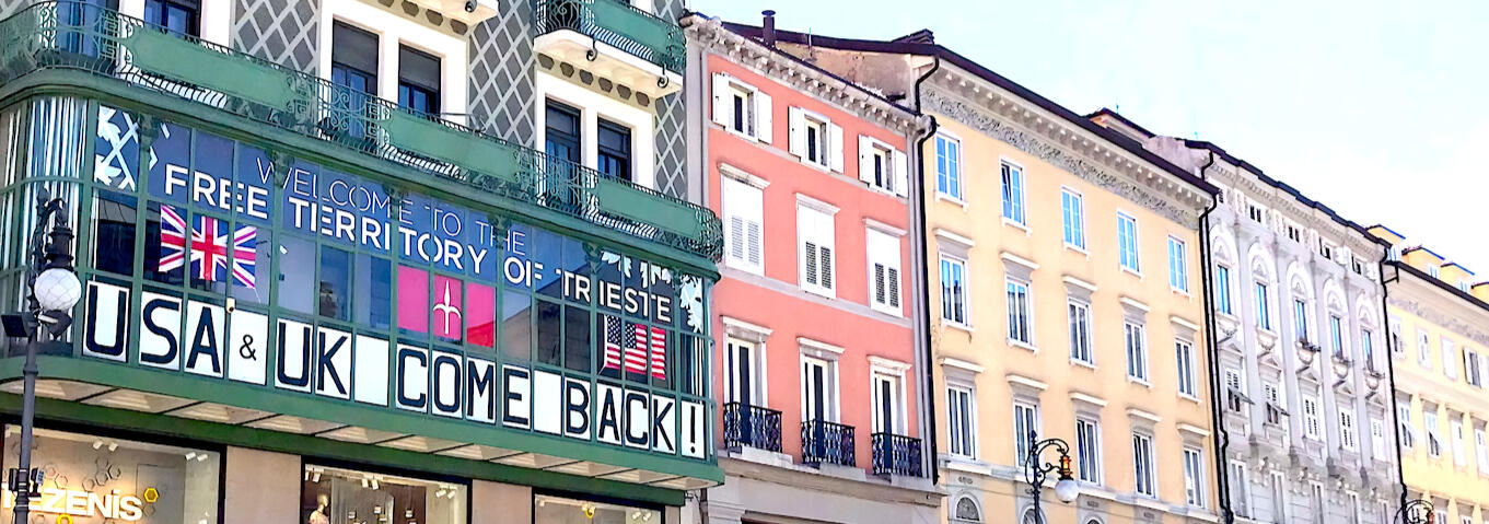 Veranda della sede di Trieste Libera, in Piazza della Borsa 7, Trieste. Sono esposti i cartelli con la scritta "Welcome to the Free Territory of Trieste" (benvenuti nel Territorio Libero di Trieste), le bandiere del Regno Unito, del Free Territory of Tries